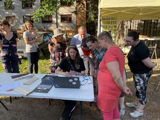 Hulk inimesi laua ümber tutvumas arvutis buildesti projektiga, taustal buildesti logoga bänner